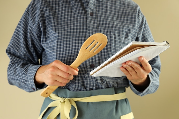 Foto la mujer sostiene el libro de recetas y una espátula de cocina sobre fondo beige
