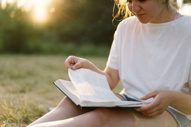 La mujer sostiene el libro en sus manos leyendo el libro en un campo durante la puesta de sol