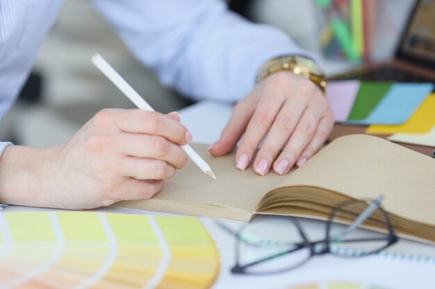 La mujer sostiene en la mano un lápiz blanco y un cuaderno en el escritorio trabajando como diseñador