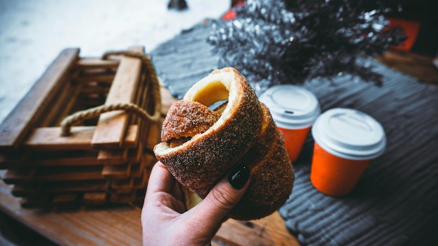 La mujer sostiene en la mano Trdlo o Trdelnik, es una comida callejera nacional de Praga en el fondo de una mesa de madera con copas de vino caliente