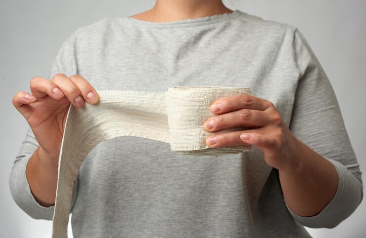 Foto la mujer sostiene en la mano un vendaje elástico blanco para el fondo gris del cuerpo