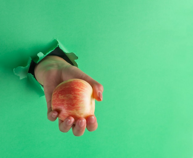 Una mujer sostiene una manzana en su mano, insertada a través de un agujero en papel verde rasgado