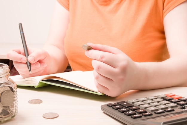 Una mujer sostiene una moneda de 10 rublos y escribe algo en un cuaderno.