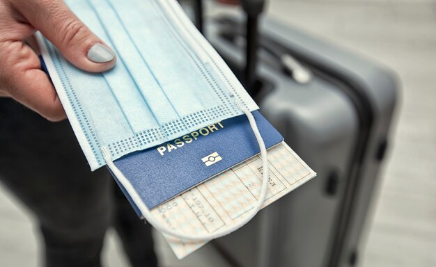 La mujer sostiene el pasaporte con el boleto de tren y la máscara médica como algo esencial en los viajes en el tiempo posterior al covid-19.