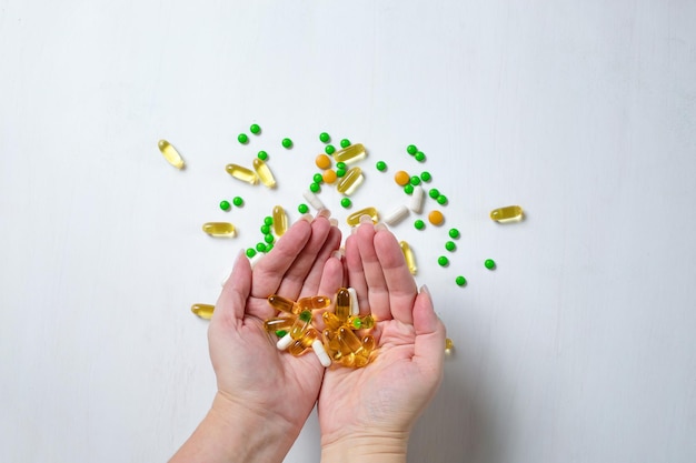 Una mujer sostiene pastillas de vitaminas en la mano sobre un fondo blanco de madera