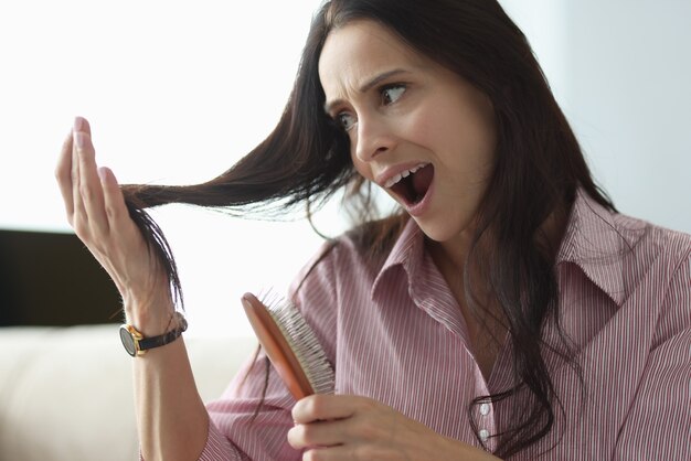 Foto la mujer sostiene el peine en la mano y mira su cabello en pánico.