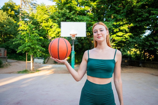 Una mujer sostiene una pelota de baloncesto en un parque y es una mujer feliz y deportiva