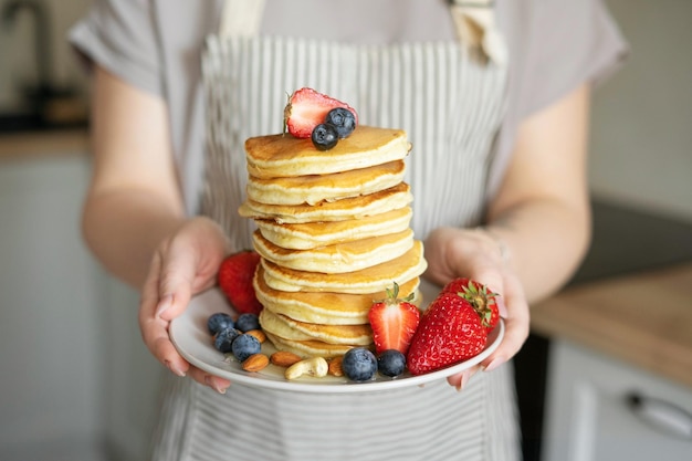 Una mujer sostiene un plato de panqueques adornados con fresas, arándanos, nueces y miel.