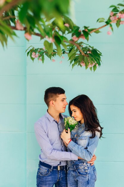 La mujer sostiene un ramo de flores y el chico la abraza. están parados cerca de la pared