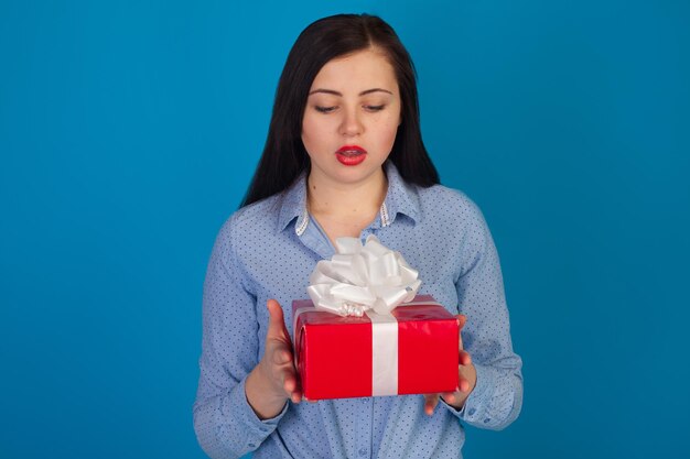 La mujer sostiene un regalo rojo en sus manos contra un fondo azul