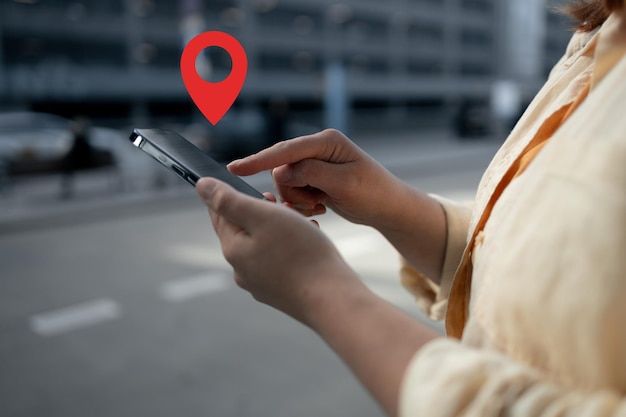 Una mujer sostiene su teléfono inteligente con el dedo en la pantalla que muestra un icono de pin de ubicación este