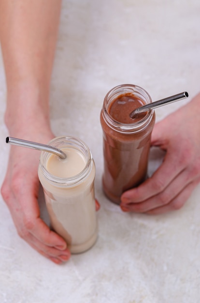 Una mujer sostiene en sus manos dos botellas de vidrio con un cóctel de proteínas (leche y cacao). Bebe una bebida con una pajita. Cuidado de la salud