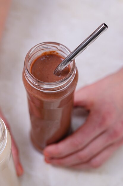 Una mujer sostiene en sus manos dos botellas de vidrio con un cóctel de proteínas (leche y cacao). Bebe una bebida con una pajita. Cuidado de la salud