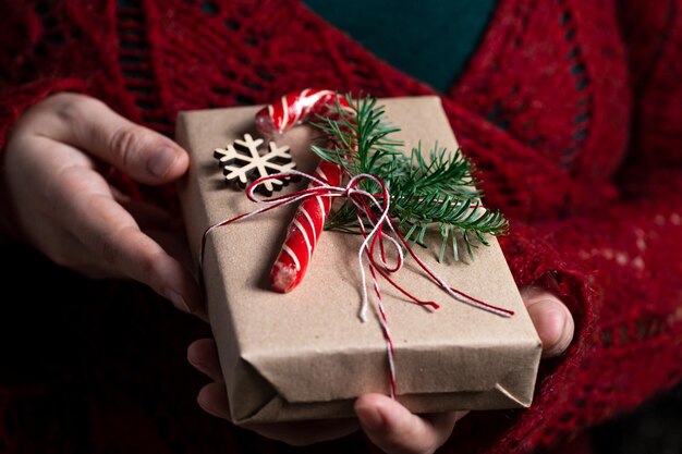 Una mujer sostiene en sus manos un regalo atado con un hilo decorado con una ramita de nobilis y un palo de caramelo