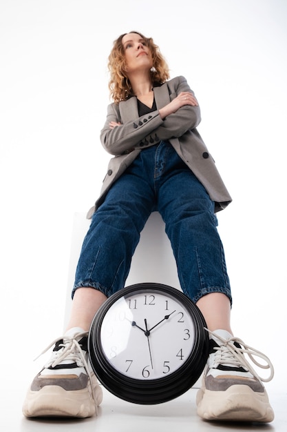 Foto una mujer sostiene entre sus piernas un gran reloj sobre un fondo blanco.