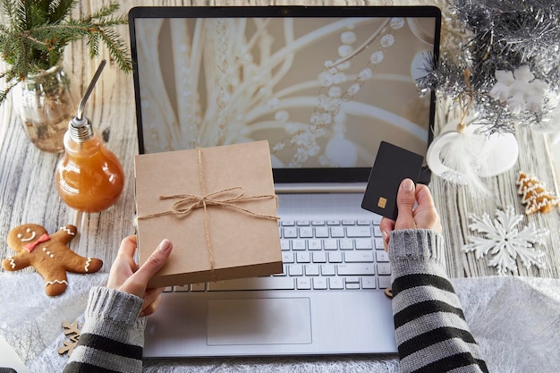 La mujer sostiene una tarjeta de pago y un regalo Buscando y comprando regalos para Navidad en línea