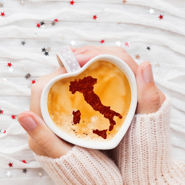 La mujer sostiene una taza de café caliente con la silueta de la canela de Italia.