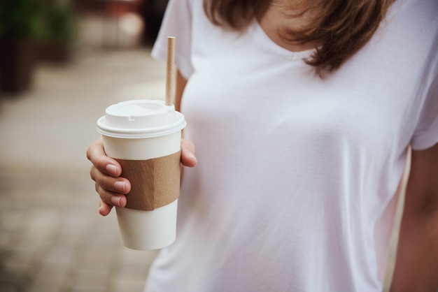 Mujer sostiene una taza de café de papel en las calles de la ciudad