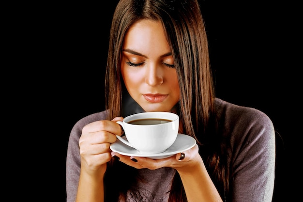 La mujer sostiene una taza de café y un plato en las manos de cerca