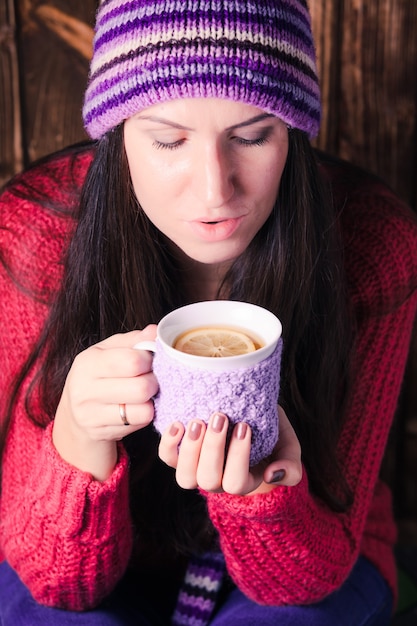 La mujer sostiene una taza de té tejida con limón