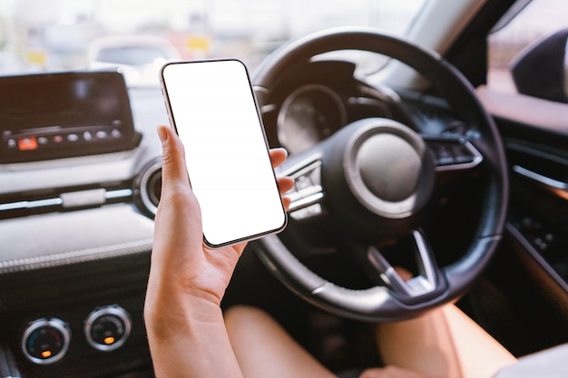 La mujer sostiene un teléfono inteligente con una maqueta en el automóvil.