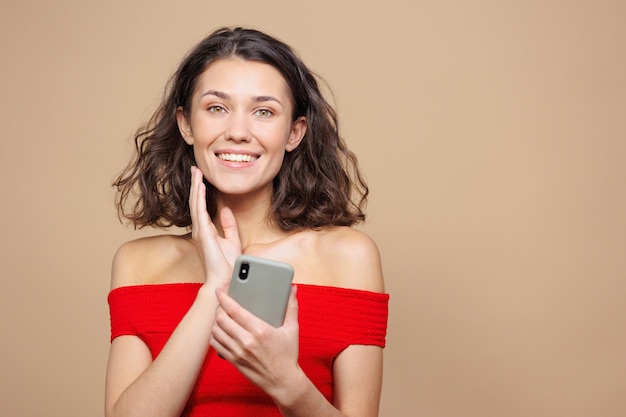 La mujer sostiene un teléfono inteligente en sus manos y llama o chatea con amigos a una mujer hermosa de fondo beige