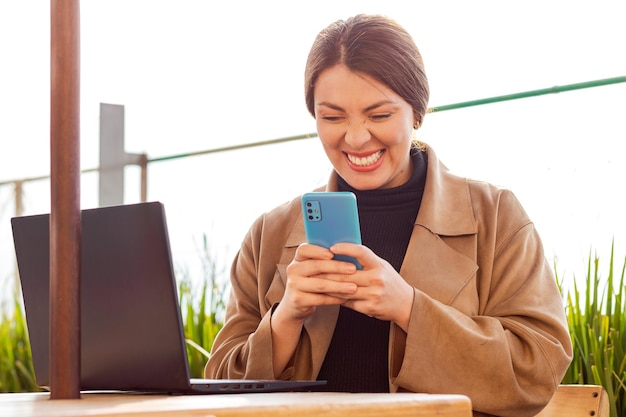 La mujer sostiene el teléfono en su cara y sonríe con emoción posiblemente recibiendo noticias positivas o ganando un premio
