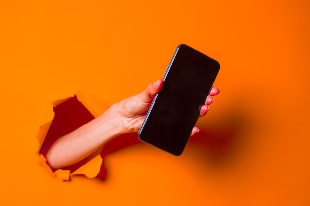 Una mujer sostiene un teléfono a través de un primer plano de fondo de papel naranja irregular