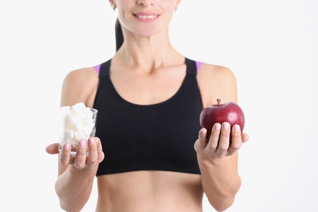 La mujer sostiene un vaso de azúcar y una manzana madura eligiendo el concepto de comida sana correcta