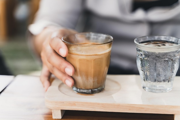 La mujer sostiene un vaso de espresso sobre leche fresca fría Café sucio Menú de café Café con leche