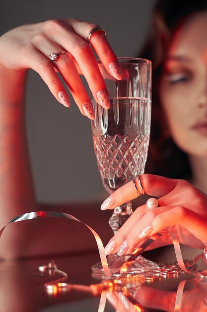 La mujer sostiene un vaso de vidrio en su mano de belleza. Anillos y joyas en la mesa, vida lujosa. Alcoholismo