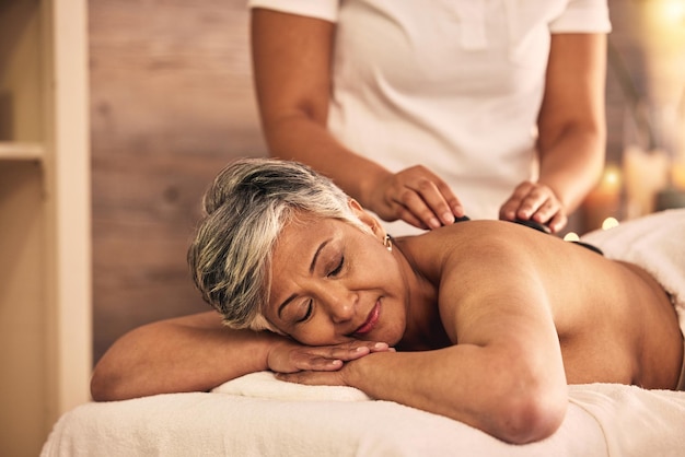 Mujer spa y masaje con piedras para curar el tratamiento de cuidado de la piel de los músculos de la espalda y terapia holística en el salón de belleza Mujer madura relajarse en el centro de bienestar con rocas para el autocuidado desintoxicación y zen