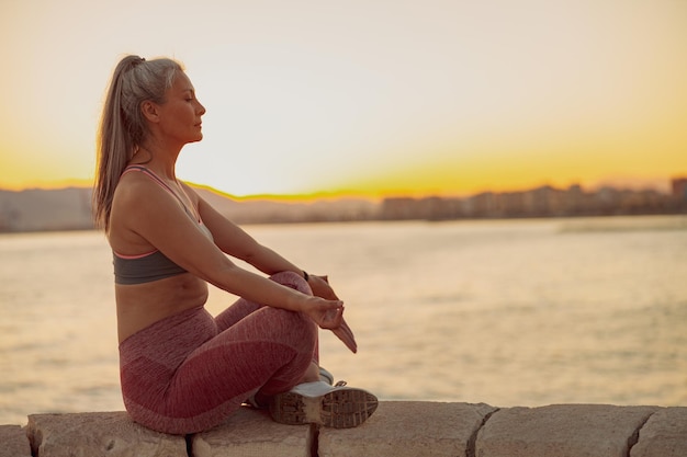 Mujer en sportewear meditando en posición de loto en la playa