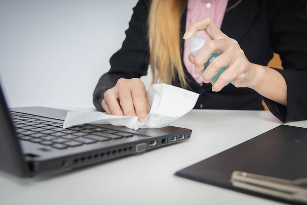 Mujer con spray de alcohol para limpiar la computadora portátil y la oficina