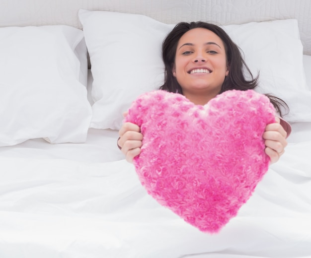 Mujer en su cama con un cojín de corazón esponjoso