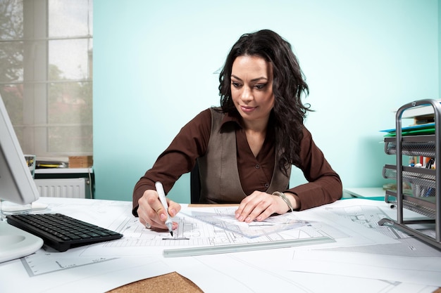 Mujer en su escritorio de trabajo con planos frente a ella. Trabajando en nuevos proyectos. Arquitectura y Diseño