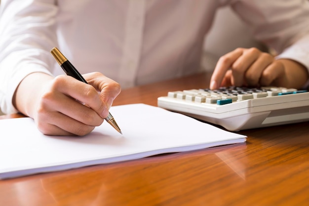 Una mujer en su escritorio usando una calculadora y escribiendo en papel blanco