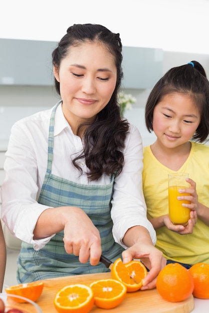 Mujer con su hija joven cortar fruta en la cocina