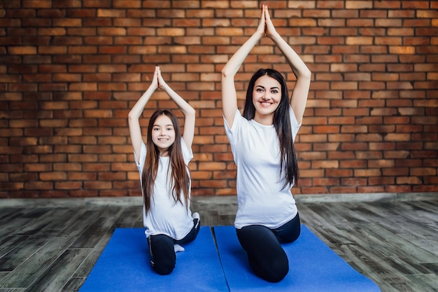 Mujer y su hija practicando yoga y meditación en casa, tumbadas en el suelo y haciendo la pose.