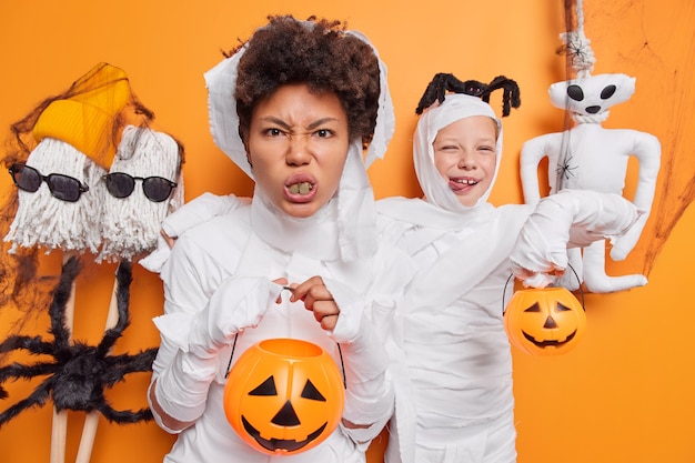 Mujer y su hija se preparan para la fiesta de Halloween celebrar atributos de vacaciones visten trajes de zombies blancos aislados en estudio naranja