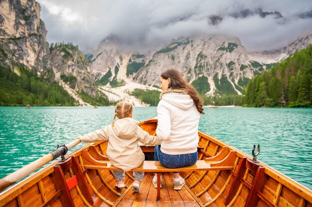 Mujer con su hija sentada en un gran barco marrón en el lago di braies en un día nublado italia