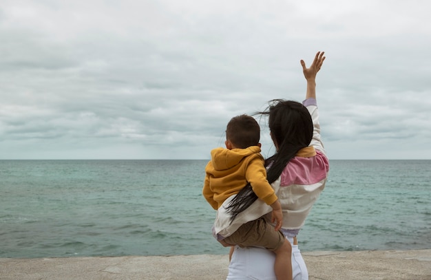 Mujer con su hijo en brazos, saludando al mar