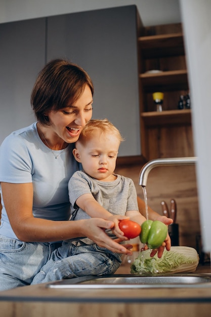 Foto mujer con su hijo lavando verduras en el fregadero de la cocina
