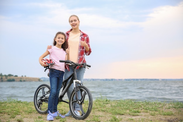 Mujer y su pequeña hija con bicicleta cerca del río