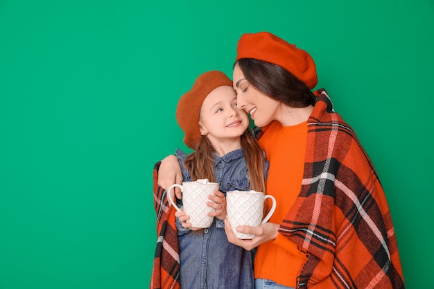 Mujer y su pequeña hija con sabrosa bebida de cacao sobre fondo de color