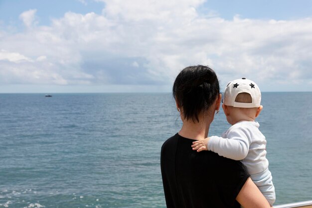 Una mujer y su pequeño hijo contra un cielo azul con nubes y el mar