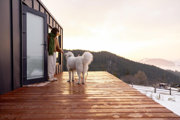 Mujer con su perro descansando en la terraza de una pequeña casa en la naturaleza