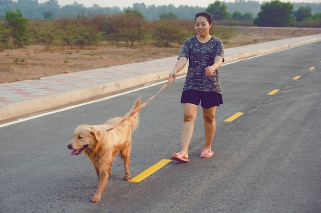 Mujer con su perro del golden retriever que camina en el camino público.