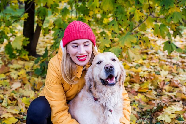 Mujer con su perro perdiguero en el parque de otoño entre hojas amarillas.