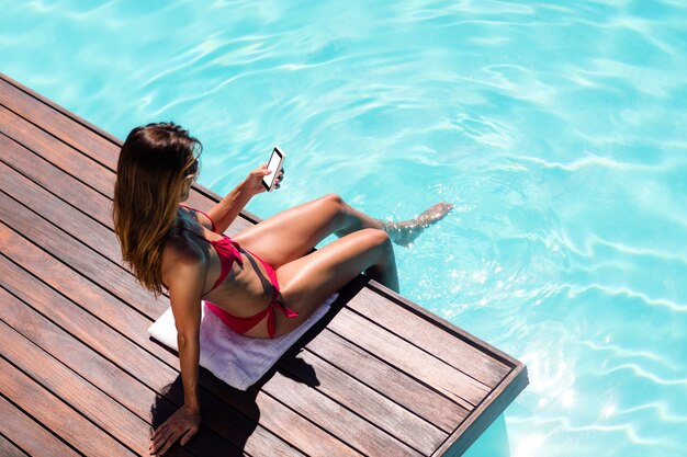 Foto mujer con su teléfono inteligente en el borde de la piscina